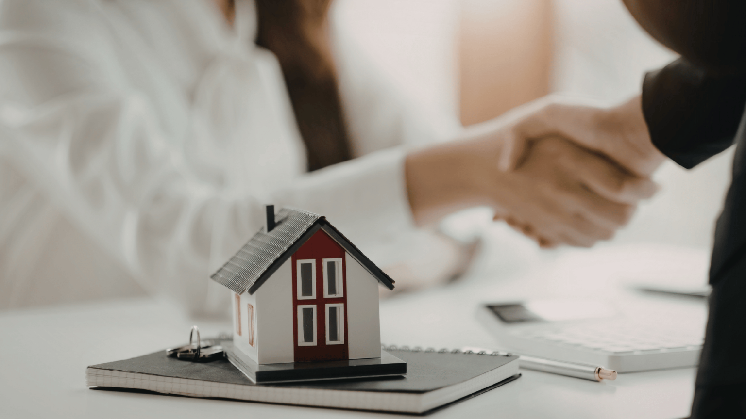 Handshake over a model home, representing a closed deal